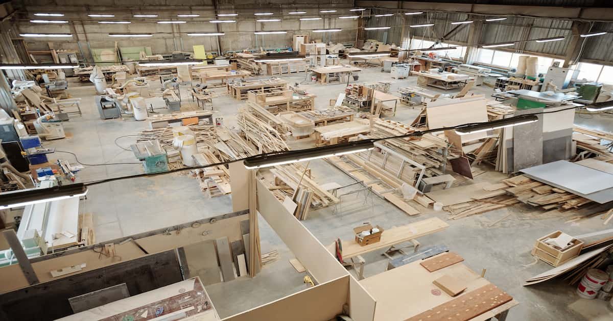 An expansive modular office furniture factory with woodworking machinery, raw materials, and workstations, showcasing the large-scale production process.